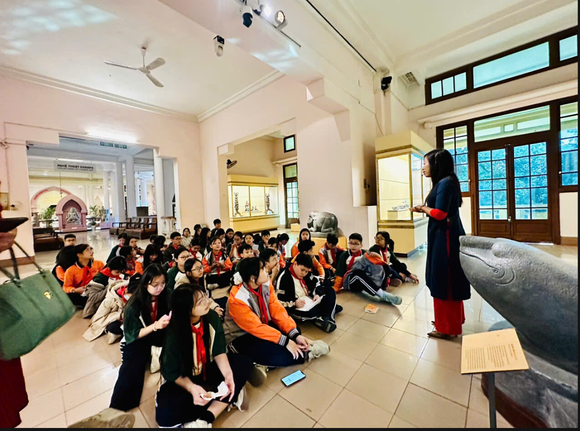 A group of people sitting on the floor in a room with a person standing in front of a statue
AI-generated content may be incorrect.